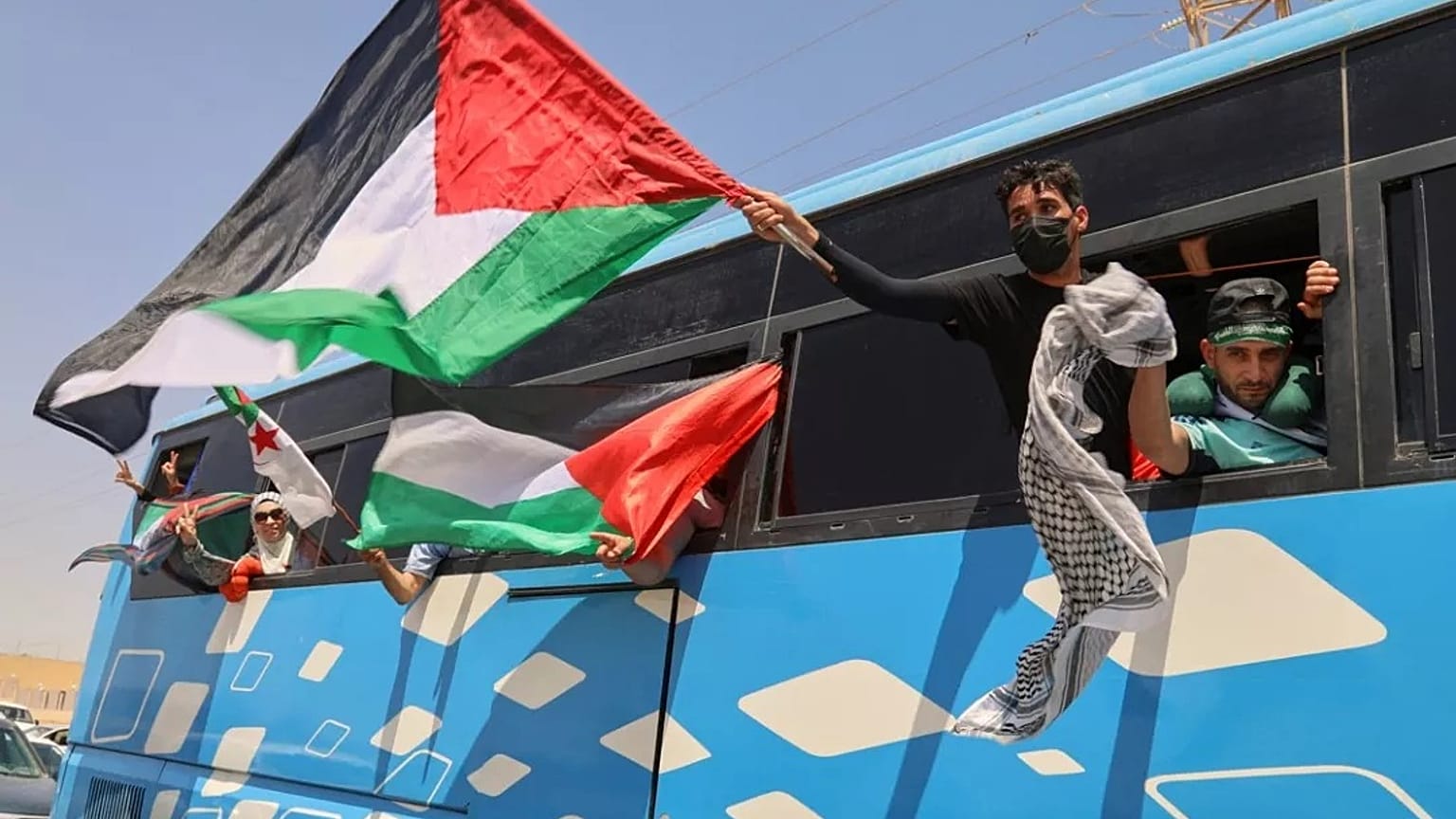 يلوح أعضاء قافلة إنسانية تضم ما لا يقل عن 1500 شخص، بالأعلام الفلسطينية من على متن حافلة أثناء توجه المجموعة إلى غزة، الثلاثاء 10 يونيو/حزيران 2025.