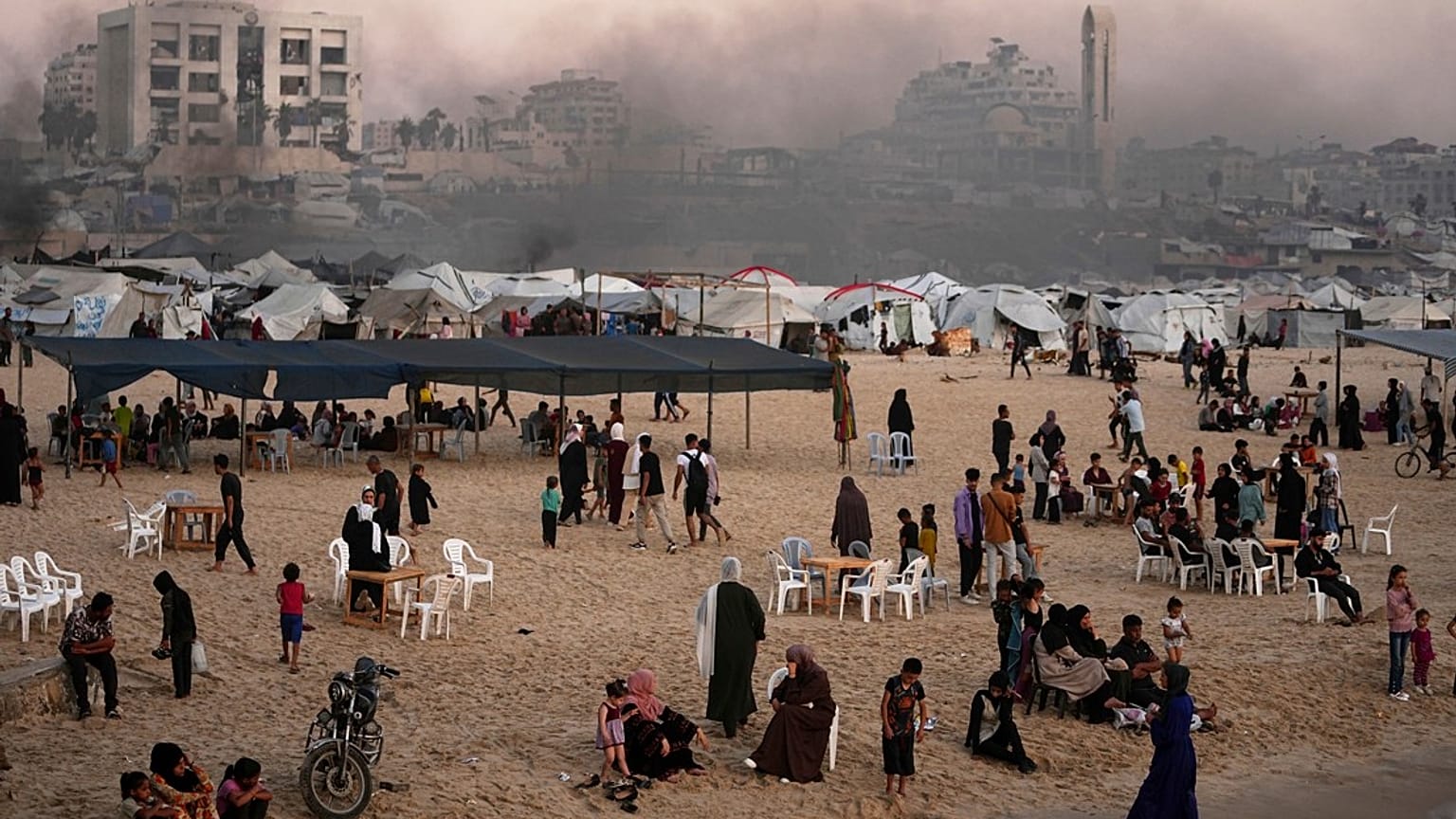 فلسطينيون يقضون وقتهم على شاطئ البحر بجوار مخيم في ميناء مدينة غزة، الجمعة 13 يونيو 2025. 