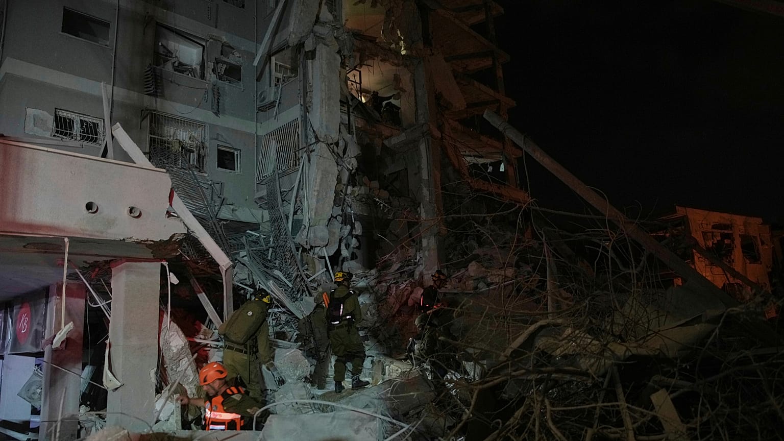 İsrail güvenlik güçleri, 15 Haziran 2025, Pazar günü erken saatlerde İsrail'in Tel Aviv kenti yakınlarında İran'dan atılan bir füzenin isabet ettiği yıkık binaları inceliyor.