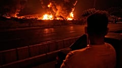 رجل ينظر إلى ألسنة اللهب المتصاعدة من منشأة لتخزين النفط بعد أن بدا أنها تعرضت لضربة إسرائيلية في طهران، إيران، في وقت مبكر من يوم الأحد، 15 يونيو / حزيران 2025