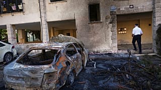 Мужчина проходит мимо горящих автомобилей на месте падения иранской ракеты в Хайфе, Израиль, понедельник, 16 июня 2025 года.