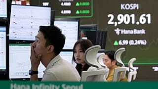 A currency trader watches monitors near a screen showing the Korea Composite Stock Price Index (KOSPI) .