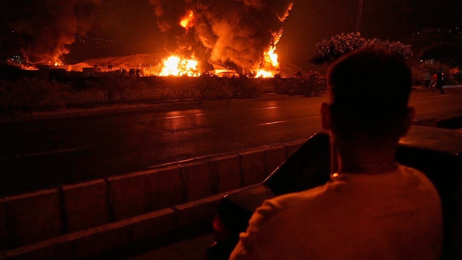 Ein Mann betrachtet die Flammen, die nach einem israelischen Angriff in Teheran, Iran, am Sonntag, 15. Juni 2025, aus einem Öllager aufsteigen.  