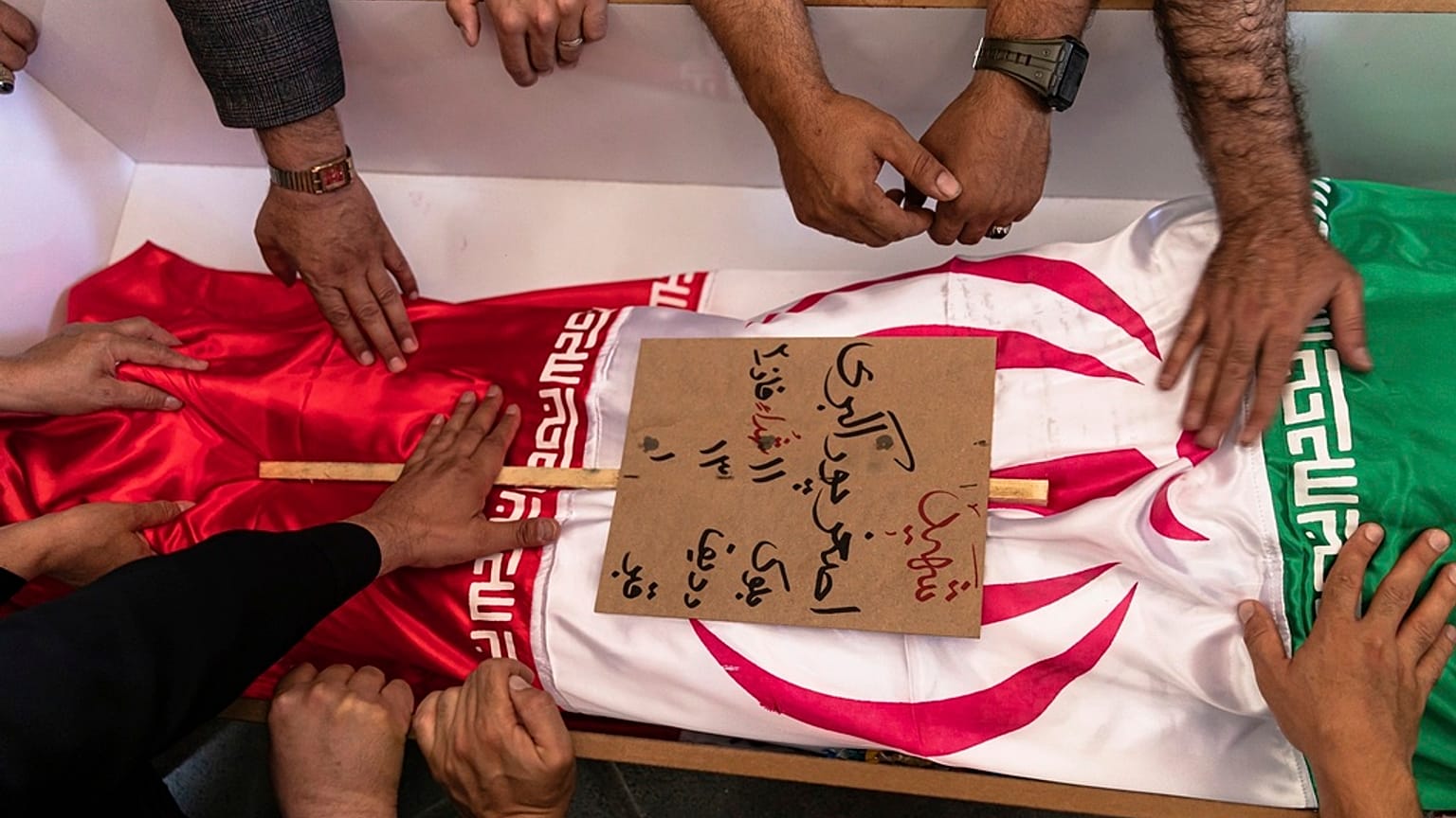 مشيعون يلمسون جثمان أصغر بوراكبري المسجى بالعلم الإيراني والذي قيل إنه قُتل خلال الغارات الإسرائيلية في مدينة تبريز شمال غرب إيران، الاثنين، 16 يونيو/حزيران 2025