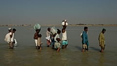 Túlélők gázolnak a vízben a pakisztáni Khairpur Nathan Shah falujukban 2010. november 2-án, amelyet árvíz vesz körül.