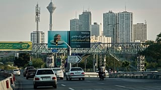 Vehicles drive on a highway with residential towers and the Milad telecommunications tower visible in the background in northern Tehran, Iran, Friday, June 13, 2025.