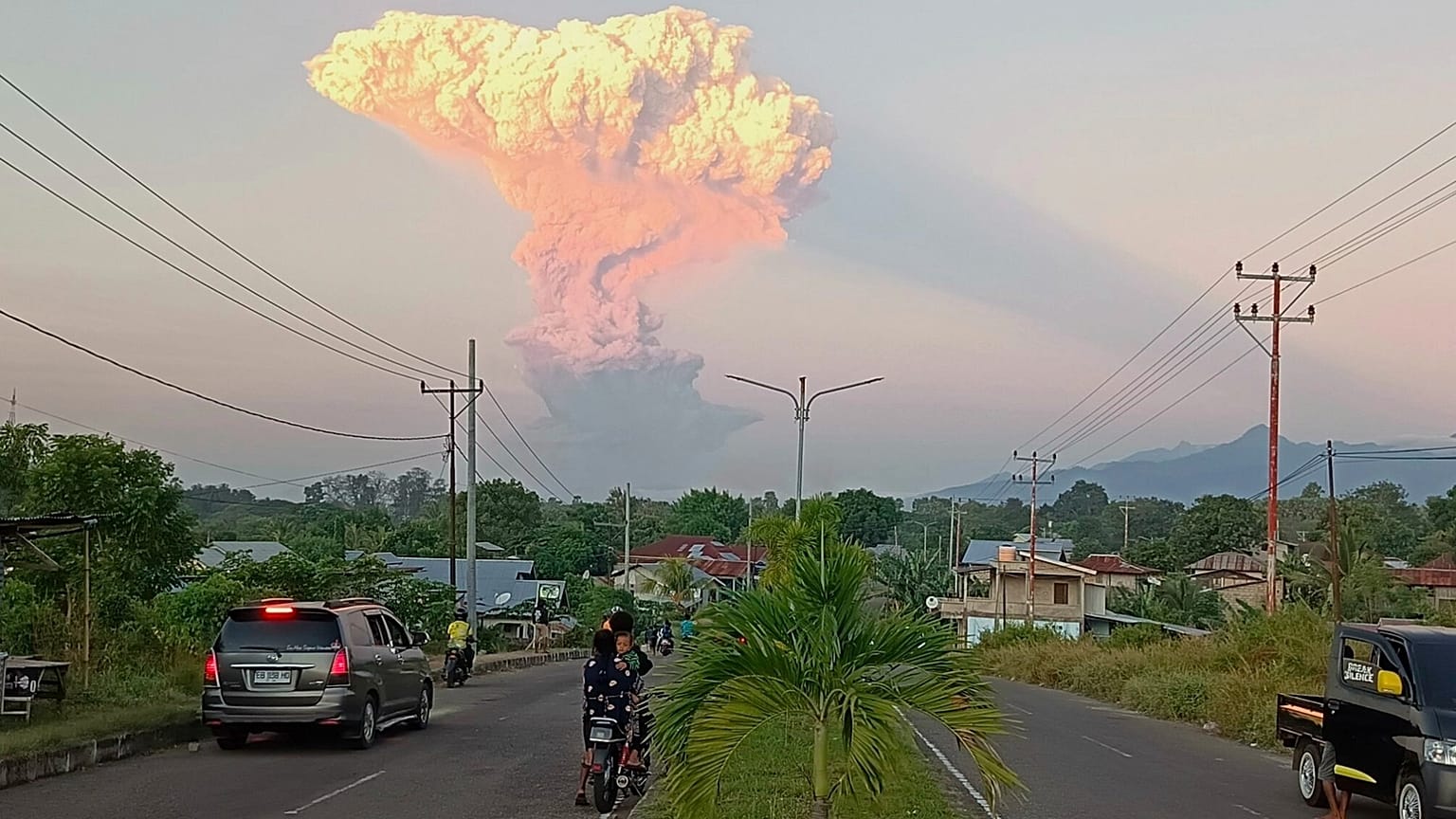 Menschen beobachten in Maumere, Indonesien, wie der Berg Lewotobi Laki-Laki während eines Ausbruchs vulkanisches Material in die Luft spuckt.