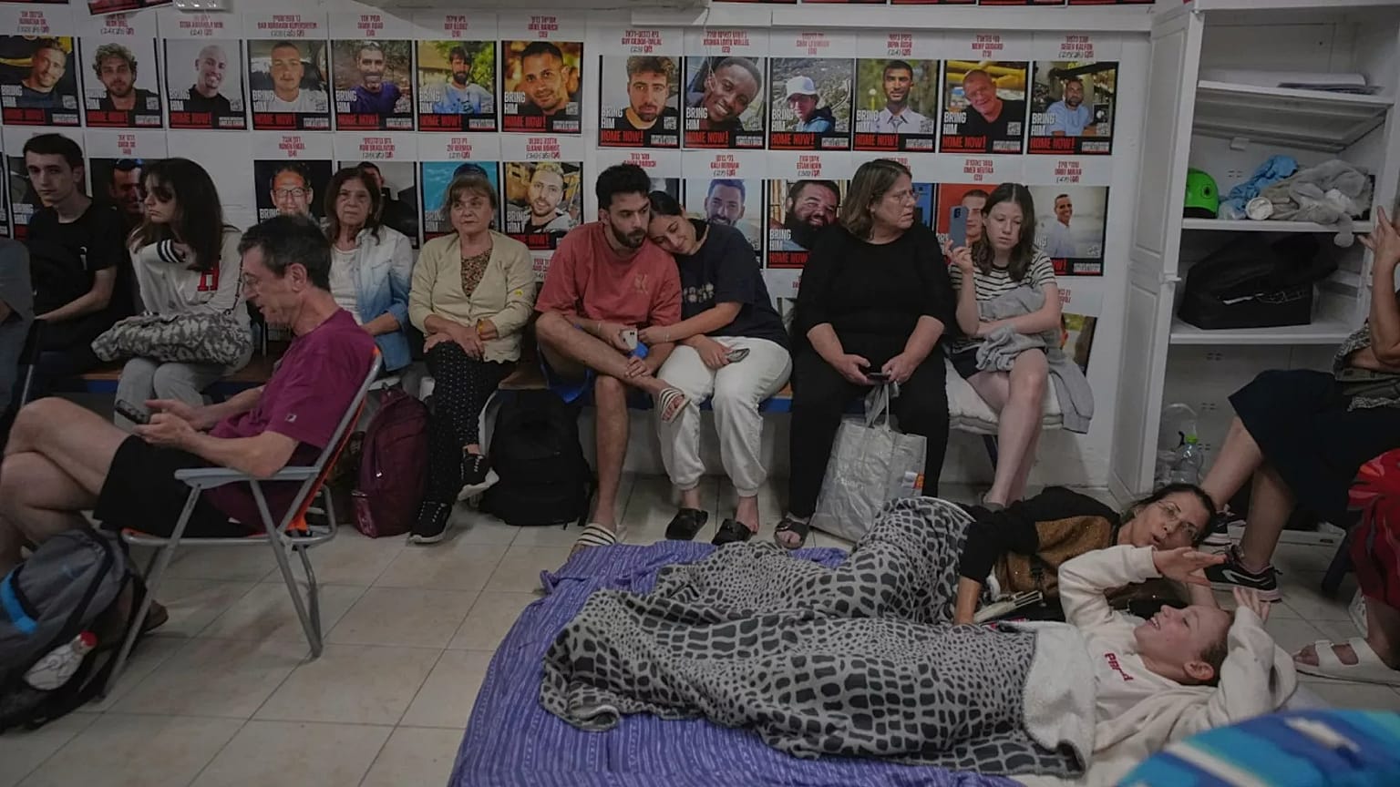 Pessoas abrigam-se junto a fotografias de reféns israelitas raptados durante o ataque do Hamas, durante as sirenes dos ataques aéreos que avisam da aproximação de ataques do Irão, 19 de junho de 2025.