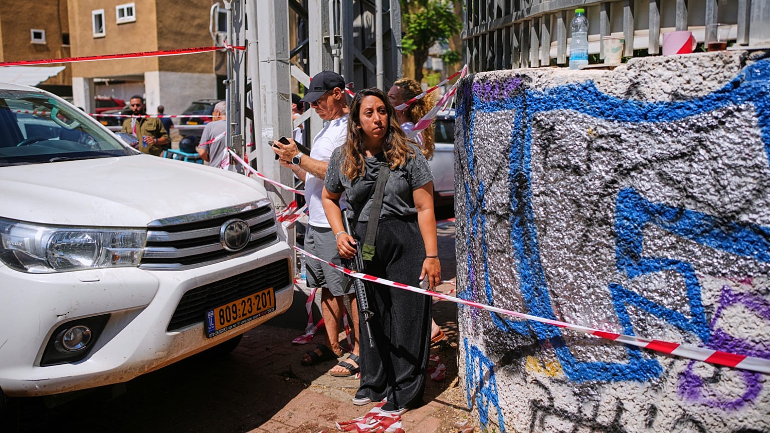 Bir kadın, 19 Haziran 2025 Perşembe günü, Tel Aviv yakınlarındaki Holon'da İran'dan ateşlenen bir füzenin isabet ettiği yıkılmış bir binanın yanında M16 tüfeğiyle duruyor.