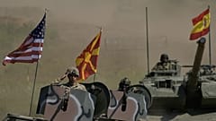 Żołnierz na czołgu salutuje, podczas gdy inne pojazdy z Macedonii Północnej i Hiszpanii podążają za nim podczas ćwiczeń wojskowych "Immediate Response 25", 4 czerwca 2025 r.