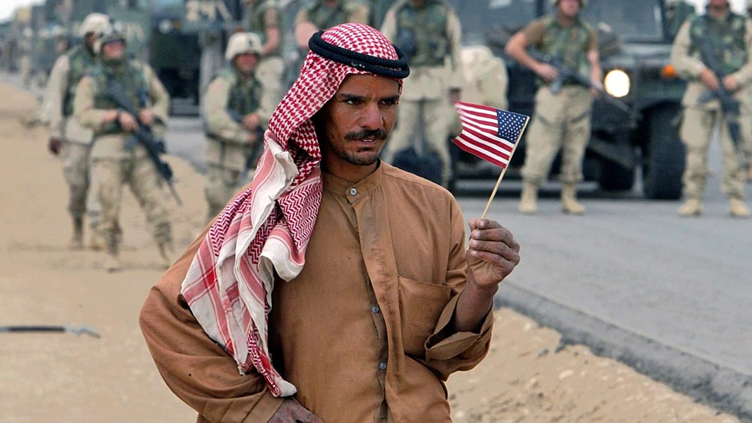 رجل عراقي يحمل العلم الأمريكي أثناء انتظاره على الطريق للترحيب بالقوات الأمريكية المتجهة إلى بغداد، جنوب العراق، يوم الاثنين 21 أبريل 2003.  