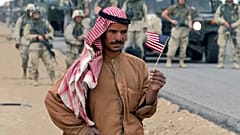رجل عراقي يحمل العلم الأمريكي أثناء انتظاره على الطريق للترحيب بالقوات الأمريكية المتجهة إلى بغداد، جنوب العراق، يوم الاثنين 21 أبريل 2003.  