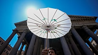 Un uomo si ripara dal sole con un ombrello di carta davanti al Pantheon di Roma durante un'ondata di calore, 11 luglio 2024