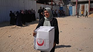 امرأة فلسطينية تحمل طردًا غذائيًا وزّعته منظمة "أنيرا" للإغاثة في مدينة غزة، 26 حزيران/يونيو 2025.