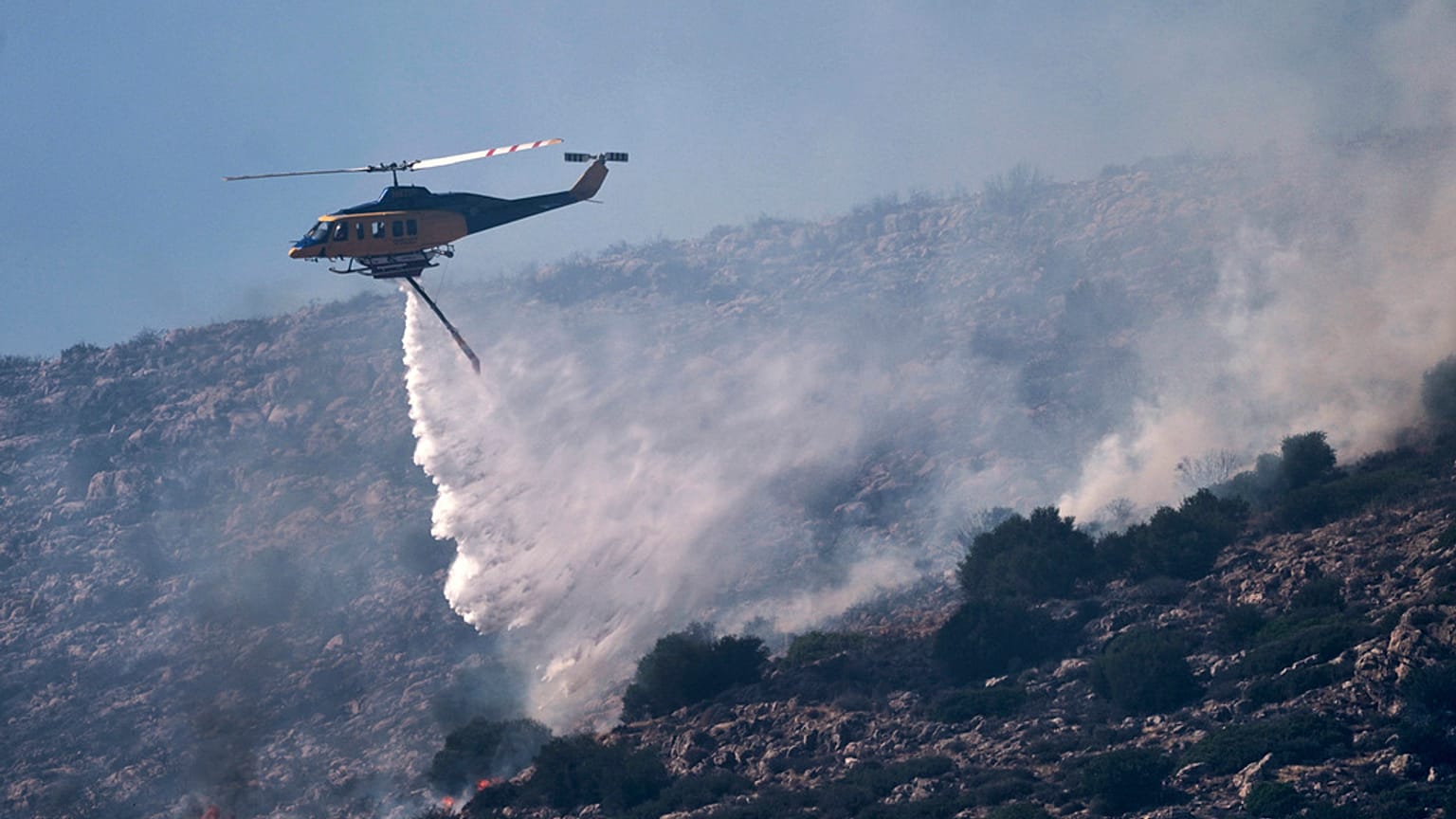 Πυροσβεστικό ελικόπτερο ρίχνει νερό κατά τη διάρκεια κατάσβεσης πυρκαγιάς στην παραθαλάσσια περιοχή του Χάρακα, νότια της Αθήνας, Πέμπτη 26 Ιουνίου 2025,
