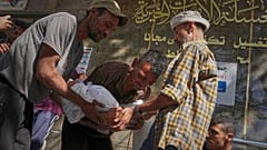 رجل يحمل جثة طفل ملفوفة لطفل قُتل مع آخرين في غارة إسرائيلية استهدفت مدرسة في شمال قطاع غزة، في مستشفى الشفاء في مدينة غزة، الجمعة، 27 يونيو 2025.