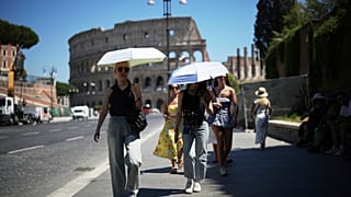 Le persone usano gli ombrelli per ripararsi dal sole mentre passeggiano davanti al Colosseo, a Roma, 30 giugno 2025
