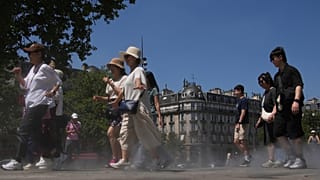 Τουρίστες περπατούν μέσα από δροσερό νερό που ψεκάζεται στο έδαφος κατά τη διάρκεια ενός τεστ ψεκασμού, κατά τη διάρκεια ενός κύματος καύσωνα τη Δευτέρα, 30 Ιουνίου 2025 στο Παρίσι