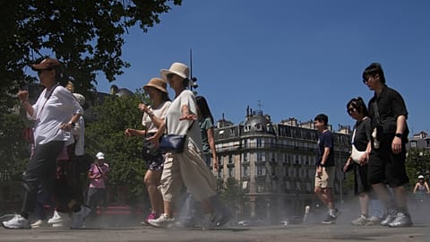 Des touristes marchent à travers une brume d'eau fraîche vaporisée sur le sol lors d'un test de brumisateur, pendant une vague de chaleur, lundi 30 juin 2025 à Paris