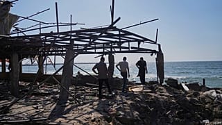 فلسطينيون يسيرون في مقهى بعد أن تضرر جراء غارة إسرائيلية في مدينة غزة، يوم الاثنين 30 يونيو/حزيران 2025.