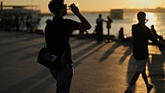 Menschen trinken Wasser an einem heißen Sommertag an der Strandpromenade von Kadikoy in Istanbul, Türkei, Mittwoch, 2. Juli 2025.