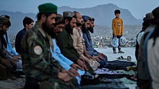Combatentes talibãs rezam na colina de Nader Khan enquanto uma criança observa, em Cabul, Afeganistão, terça-feira, 10 de junho de 2025.  