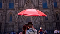 Ein Paar schützt sich mit einem Regenschirm vor der Sonne, während es die Kathedrale von Barcelona betrachtet.