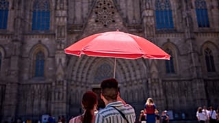 Una pareja se protege del sol con una sombrilla mientras contempla la catedral de Barcelona.