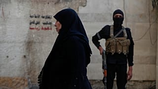 امرأة سورية تمشي أمام رجل أمن حكومي سوري ، خارج مرقد السيدة زينب ، حفيدة النبي محمد ، حيث يحضر المصلون الشيعة طقوس عاشوراء ، جنوب دمشق ، سوريا ، الخميس ، 3 يوليو ، 2025.