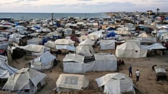 Palestinians displaced by the Israeli air and ground offensive on the Gaza Strip, stand in an area at a makeshift tent camp at dusk in Khan Younis, Gaza Strip, Wednesday