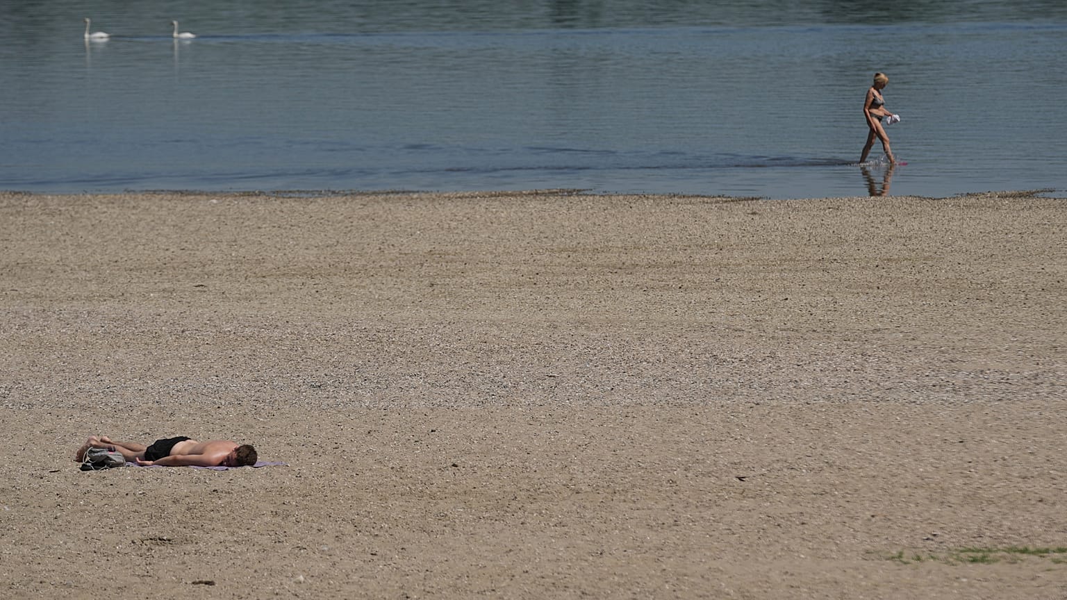 Une femme patauge dans le Danube tandis qu'un homme prend un bain de soleil sur la rive pendant une chaude journée d'été à Belgrade, Serbie, jeudi 3 juillet 2025.