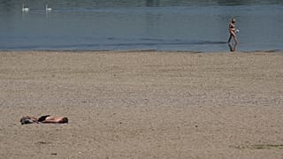 Une femme patauge dans le Danube tandis qu'un homme prend un bain de soleil sur la rive pendant une chaude journée d'été à Belgrade, Serbie, jeudi 3 juillet 2025.
