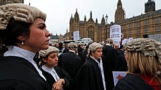 Ügyvédek plakátokat tartanak, miközben részt vesznek a jogi segítségnyújtás csökkentése elleni tüntetésen a londoni Parlamenttel szemben. 2014. március 7.