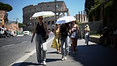 Menschen benutzen bei heißem Wetter Regenschirme, um sich vor der Sonne zu schützen, während sie am Kolosseum vorbeigehen, in Rom, Montag, 30. Juni 2025. (AP Photo/Andrew Medichini)