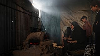 Palestinianos deslocados cozem pão numa escola agora utilizada como abrigo em Deir al-Balah, Faixa de Gaza, domingo, 6 de julho de 2025.
