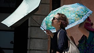 Women walk with umbrellas to shelter from the sun in hot weather, near Castle Square in Warsaw. 3 July 2025.