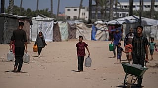 فلسطينيون يحملون حاويات مياه في مخيم للنازحين في دير البلح بقطاع غزة، الاثنين 7 يوليو/تموز 2025.  
