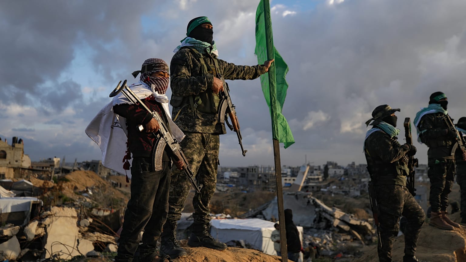 DATEI: Ein Junge hält ein AK-47-Gewehr in der Hand, während er neben einem militanten Hamas-Anhänger steht, bevor die vier Leichen von Geiseln dem Roten Kreuz in Khan Younis übergeben werden, 20. Februar 2025