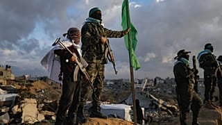 ARQUIVO: Um rapaz segura uma espingarda AK-47 ao lado de um militante do Hamas antes da entrega de quatro corpos de reféns à Cruz Vermelha em Khan Younis, 20 de fevereiro de 2025
