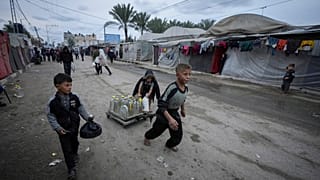 أطفال فلسطينيون يدفعون عربة تحمل صفائح المياه وزجاجات المياه البلاستيكية في مخيم للنازحين في دير البلح بقطاع غزة