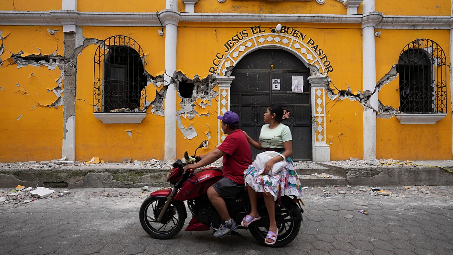 Una pareja pasa junto a un centro comunitario dañado como resultado de decenas de terremotos y réplicas registrados en cuestión de horas, Santa María de Jesús, Guatemala, 9 de julio de 2025