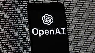 The OpenAI logo appears on a mobile phone in front of a computer screen with random binary data, March 9, 2023, in Boston