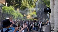 FILE - Tourists cool off near a fan as they queue to enter Rome's Colosseum, July 18, 2023. 
