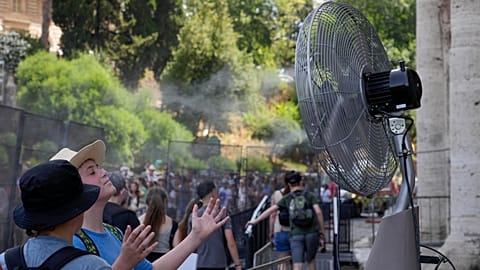 FILE - Tourists cool off near a fan as they queue to enter Rome's Colosseum, July 18, 2023. 
