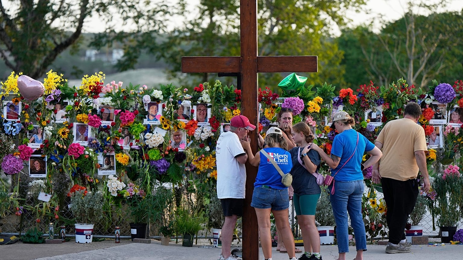 Dan Beazley, a la izquierda, sostiene una gran cruz mientras reza con los visitantes en un monumento a las víctimas de las inundaciones el jueves 10 de julio de 2025, en Kerrville, Texas.