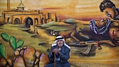  لاجئ فلسطيني أمام جدار مزين بلوحة جدارية تُصوّر الصراع الإسرائيلي الفلسطيني، الأربعاء، 18 يونيو/حزيران 2014.  