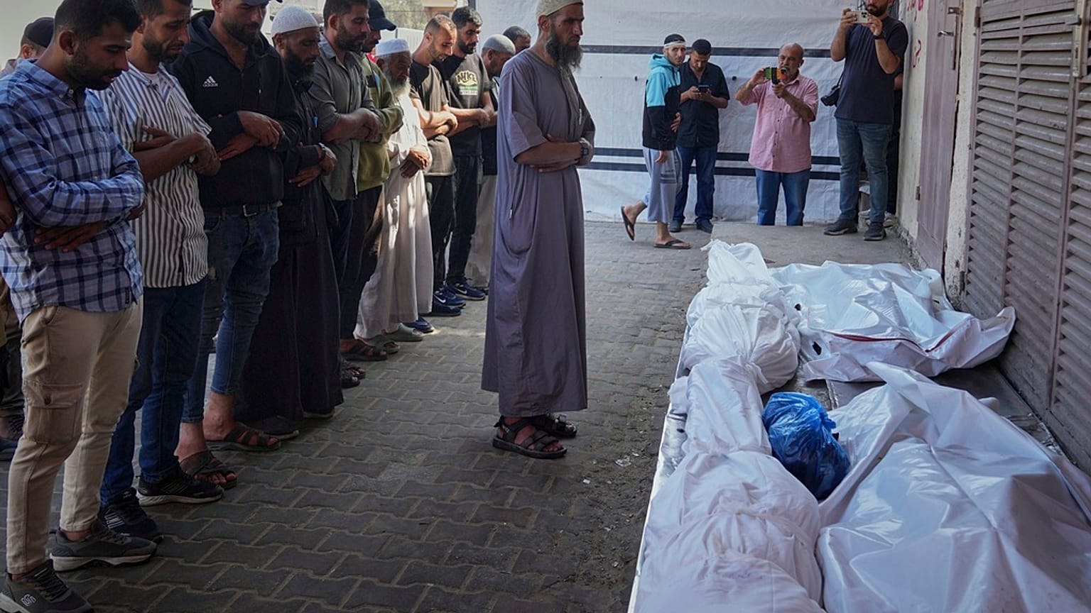 فلسطينيون يصلون على جثث 10 أشخاص، بينهم امرأتان وخمسة أطفال، قتلوا في غارة إسرائيلية أثناء انتظارهم لتلقي المكملات الغذائية في عيادة طبية تديرها مؤسسة "مشروع الأمل" في دير الب
