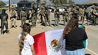 Manifestantes sostienen una bandera frente a agentes federales que bloquean una carretera durante una redada de inmigración en Camarillo, California, el 11 de julio de 2025.