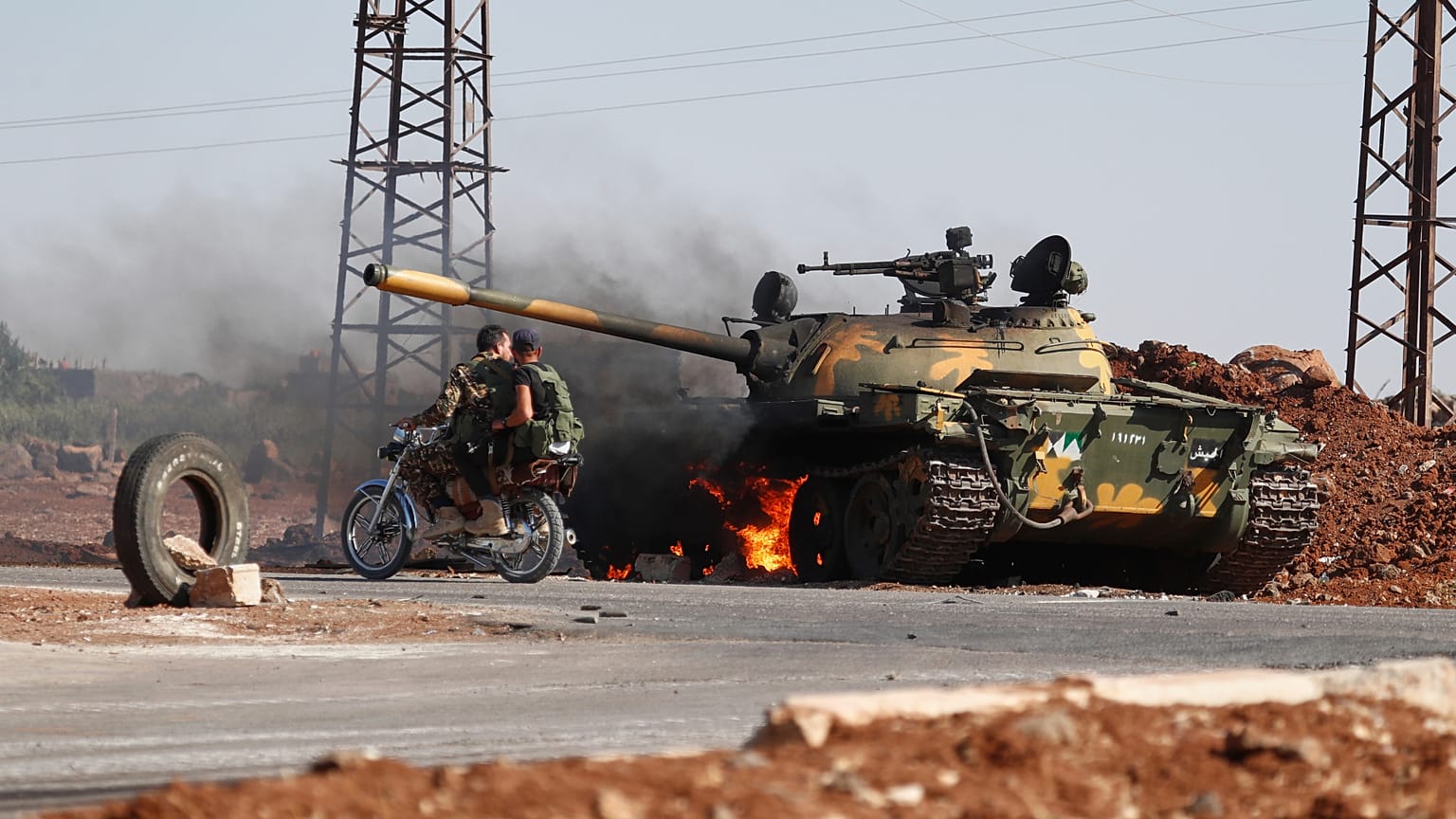Des soldats du gouvernement syrien à moto passent devant un char en flammes à la périphérie de la ville de Sweida,