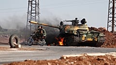 Des soldats du gouvernement syrien à moto passent devant un char en flammes à la périphérie de la ville de Sweida,
